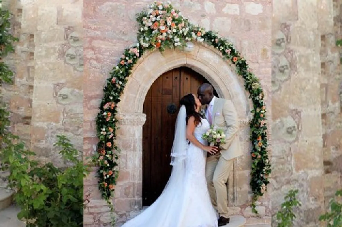 Bride and groom under a flower arch in an old stone doorway