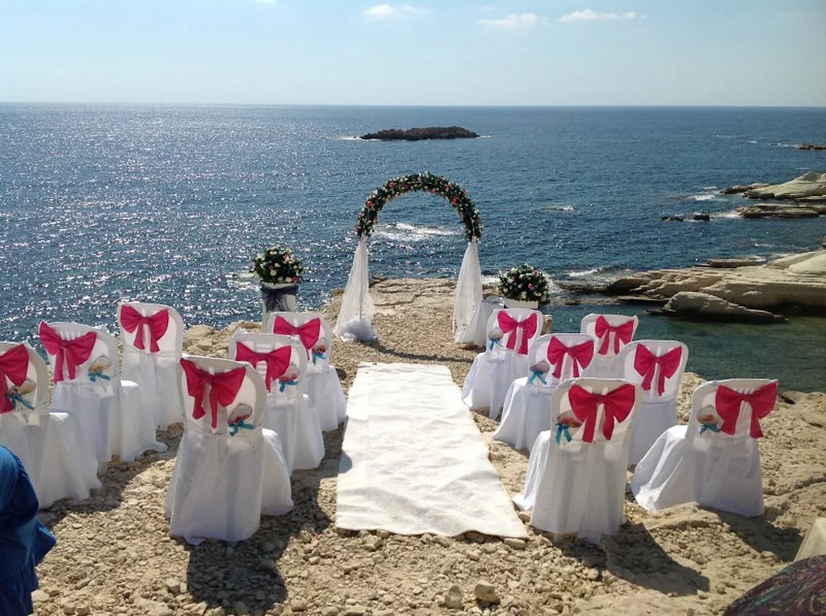 A wedding ceremony set up on the rocks above the sea with red and white chairs