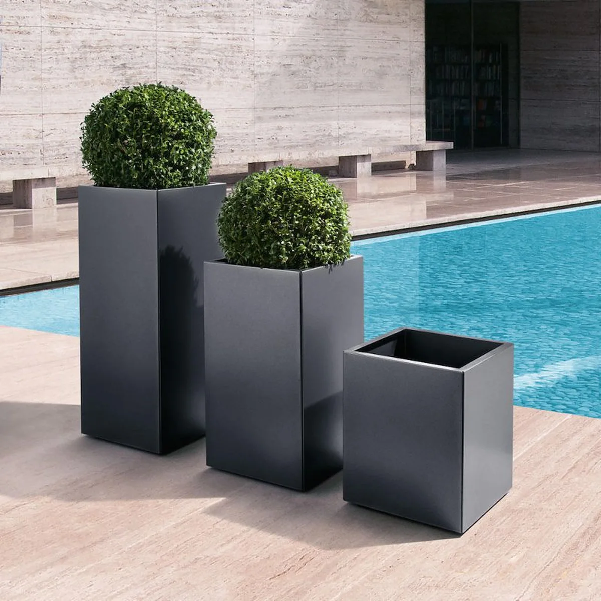 Tall dark planters with topiary balls by a pool